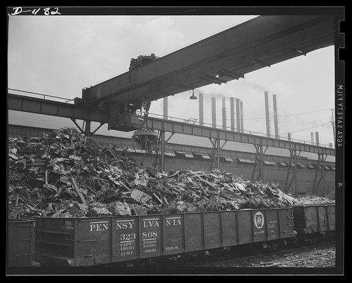 Steel manufacture, Allegheny-Ludlum. Back into production go these carloads of scrap metal. The melting of alloy steels for defense work requires that steel mill scrapyards such as this be constantly filled. The overhead magnet deposits the scrap in a loader which carries it to the open hearth furna