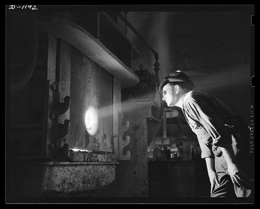 Steel manufacture, Allegheny-Ludlum. Peering through the peephole of a 25-ton electric furnace in which high quality alloy steels are being refined. Only with dark heavy glasses can melters study the action of the boiling alloy steels and determine whether adjustments are necessary to the electric p