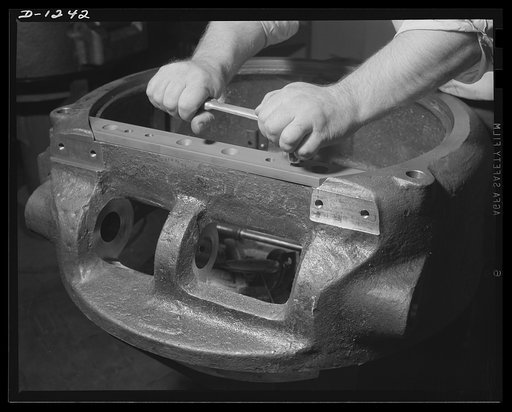 Tank manufacture (Chrysler). Ten thousand skilled workers at the huge Chrysler tank arsenal,in Detroit,turning out twenty-eight ton M-3 tanks. This pair is attaching a hinge plate to the cupola of a gun turret which will be  set on one of these rolling arsenals