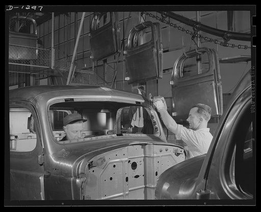 Army truck manufacture (Dodge). Many rough spots on the metal surface of the truck cab are quickly and effectively smoothed out by means of electrically operated sanders or buffers such as that being operated by the metal finisher at the right. Note the cab doors being delivered to their proper plac