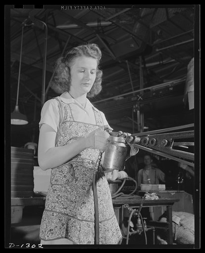 Army truck manufacture (Dodge). An attractive young lady operating an ingenious machine contributes her share to defense production. With a specially designed "gun" this girl sprays cement inside a "U" shaped rubber channel into which the glass for the rear window of truck cabs is inserted. The rubb