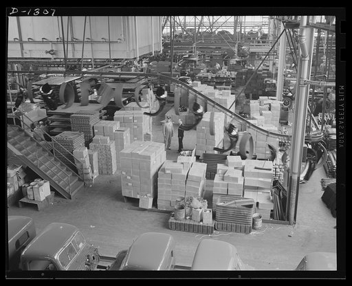 Army truck manufacture (Dodge). General view taken from above the cab-trim line in the huge Detroit plant where Dodge Army trucks are made. The camera was pointed toward the main assembly line and shows an overhead sheet metal delivery conveyor and a small portion of the parts stock, such as head la
