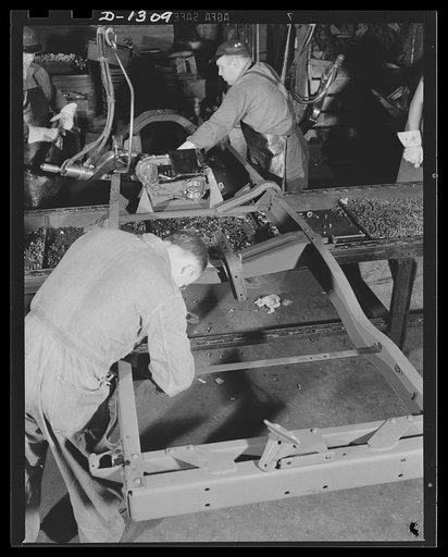 Army truck manufacture (Dodge). Defense workers in Detroit assembling the transfer case of Dodge Army truck frame assembly. Power to drive the front wheels of the army trucks is transmitted through the transfer case