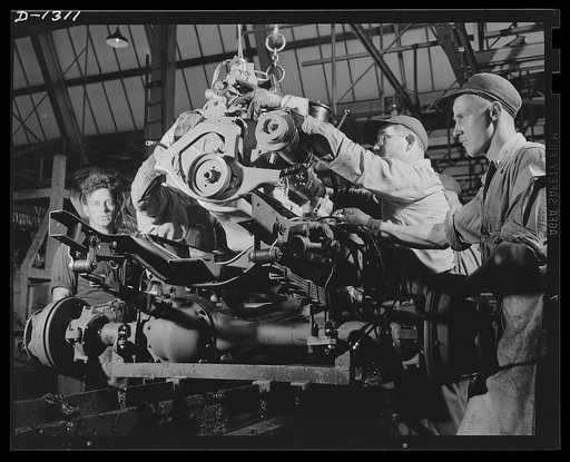 Army truck manufacture (Dodge). Dropping the power plant of a Dodge Army truck to its place in the chassis assembly. The complete motor, carried on an overhead conveyor, reaches the chassis moving along the assembly line at precisely the right time and place to permit steady production of these urge