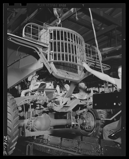Army truck manufacture (Dodge). The radiator, brush guard, and front fender assembly of a Dodge Army truck being lowered into position as the chassis moves steadily along the assembly line