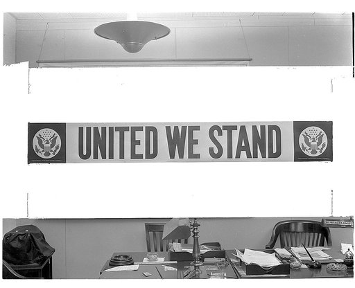 United we stand. Streamer prepared by the Office of Emergency Management (OEM) for use in defense plants throughout the nation. The poster measures 2 X 12 feet. The lettering is red against a white background, with the Great Seal of the U.S. appearing in blue