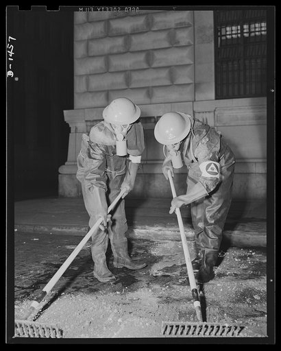 Civilian protection. Member of a decontamination squad after a raid in which blister gas has been used. Unless chemically neutralized, the spots of this liquid vesicant will continue to give off a burning vapor for days. Specially treated clothing is needed to protect the men too. Note that the work