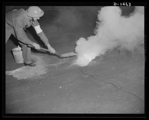 Civilian defense. The fire watcher is here shown attempting to control with sand an incendiary bomb which has just fallen. He should use a long handled shovel rather than the one shown and cover the bomb with sand after which it is quickly scooped up into a pail and carried or thrown outdoors where 