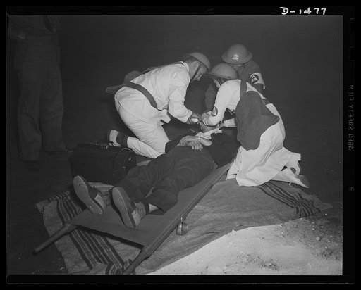 Civilian defense. No time to lose in the treatment of disaster victims. This victim is receiving attention in the field from a first aid squad. Emergency medical facilities were demonstrated at the huge October civilian defense show at Madison Square Garden, New York. The armband of the workers in t