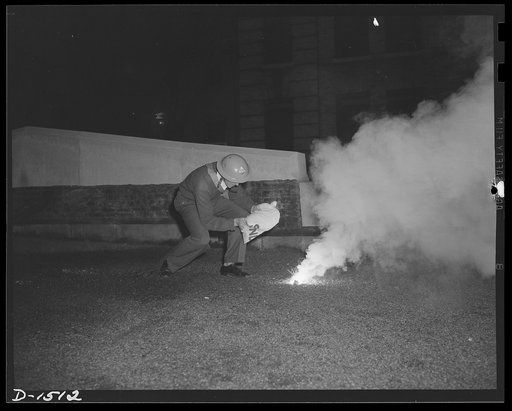 Civilian protection. This volunteer civilian defense worker, an auxiliary fireman, is preparing to extinguish an incendiary bomb. He carries the sandbag before his face to protect him from the molten magnesium sizzling forth like fat from a frying pan. He will drop the whole bag on the bomb, and the