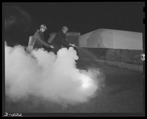 Civilian protection. Armed with carrier tanks and pressure sprays, these auxiliary firemen are disposing of an incendiary bomb by applying a fine spray of water. This accelerates the burning of the bomb and prevents the fire from spreading