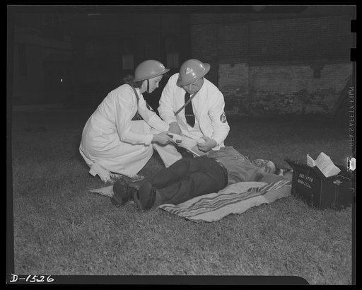Civilian protection. First Air treatment is the field to the victim of an emergency by members of a first aid group, in this case consisting of a doctor, denoted by the "M.D." and caduceus on the armband, and a nurse's aide