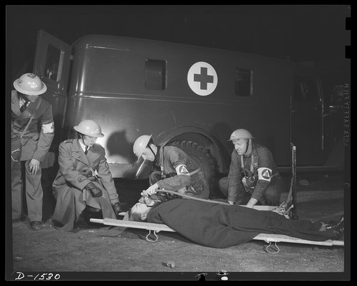 Civilian protection. Rescue workers who have brought out a victim pinned in fallen wreckage help to apply the pulmotor through by the Red Cross unit to the scene