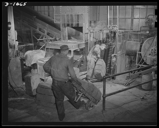 Loading raw rubber. Bales of raw rubber, removed from wooden crates in which they have traveled from Singapore, are wheeled up to this endless chain loader, which will automatically feed it into the "guillotine," the first step in making tires at an Ohio tire plant