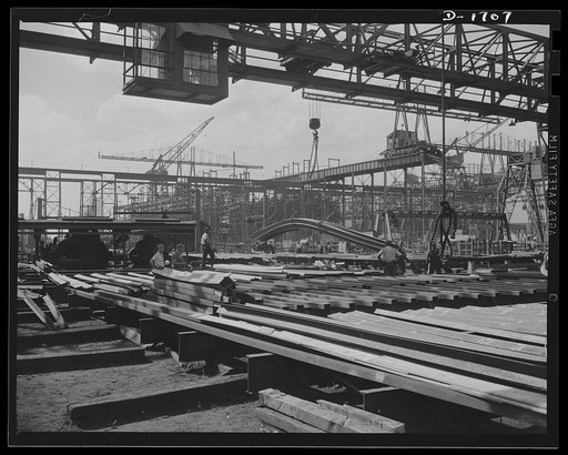 Shipbuilding (Newport News). In the foreground is the frame section for a new naval vessel under construction. The ways and overhead carriers and cranes are seen in the background