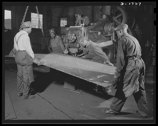Shipbuilding (Newport News). These four workers are guiding a steel plate through a punch press. When they are through, the plate will go out to the steel plate section, and thence by overhead crane to the building ways