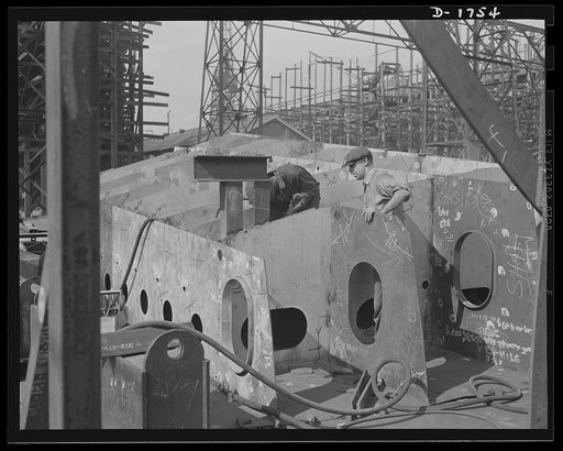 Shipbuilding (Newport News). These two workers are assembling the hull section of a new cruiser. Four new navy cruisers are on the ways here, and a huge battleship