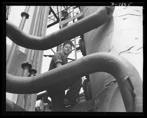 Quaker State Refining Company, Oil City, Pennsylvania. It's highly skilled work, seeing to it that the oil refined for our military machines is of the highest quality. This worker is inspecting the solution tower for denaphthizing bright stock