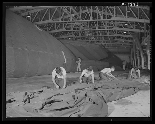 Barrage balloon manufacture. Assembling the balloon. These workers are ready to fasten one-half of a barrage balloon to the other half--the final major step in the assembly of the huge balloon. After this is done, all accessories, ropes and rigging will have to be added before the balloon can be tes