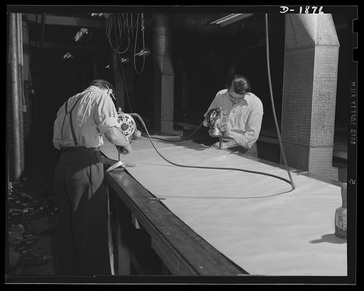 Barrage balloon manufacture. Rubber tailor shop. Using a tailor's electric cutter--a speedup suggestion from one of the young workers--these workers slice through several thicknesses of rubber fabric as they cut the patterns for the strips and "gores" for making barrage balloons. Marked, cut, assemb