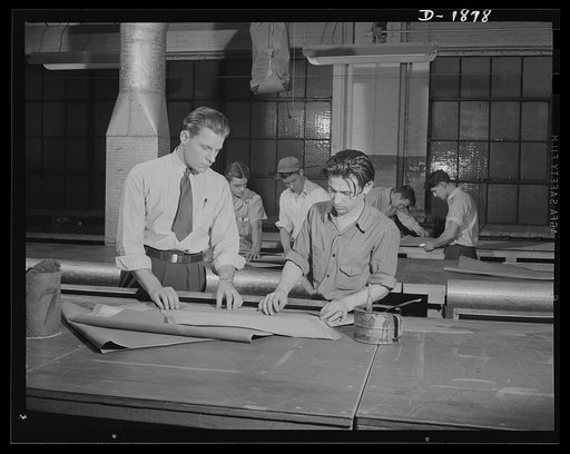 Barrage balloon manufacture. Folding instructions. Supervisor Howard Swires instructs a worker at barrage balloon department in the technique of folding fabric patterns to make efficient use of all working space. General Tire and Rubber Company, Akron, Ohio