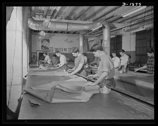 Barrage balloon manufacture. Seamers at work. Putting rubber cement on both surfaces which are to be fastened together, these workers assemble individual pattern pieces into strips or "gores" for barrage balloons being made for army balloon corps. By an ingenious arrangement of folds, strips nearly 