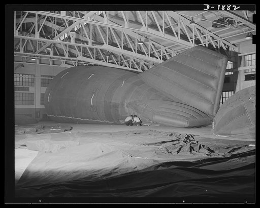 Barrage balloon manufacture. Fitting a manhold vent in the sidewall of a barrage balloon. These workers are putting in the final pieces of equipment on a completed barrage balloon, just prior to its deflation, packing and shipping to an army air base. In the foreground is a balloon ready for test in