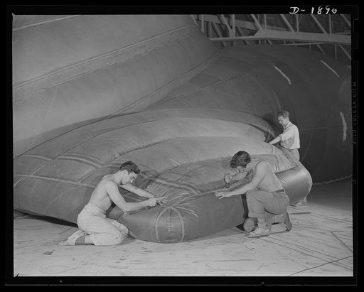 Barrage balloon manufacture. Reinforcing the fins of a fish-of-the-air. These workers at the barrage balloon division, are putting double reinforcements on the right fin of a completed barrage balloon before it is deflated and sent to army training camps Every seam must be absolutely gas- and air-ti