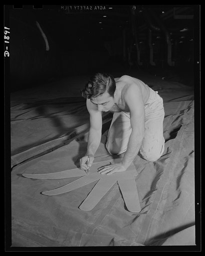 Barrage balloon manufacture. Glove for a gas bag. Fitting the outstretched fingers of a fabric patch to the side of a barrage balloon, this worker must be extremely careful to put the patch on smoothly. Any wrinkles might bind, pinch or chafe and cause leaks. Sewn and seamed inside this "glove" is a