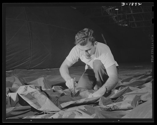 Barrage balloon manufacture. Cementing with a paint brush. This worker is a fabric cementer busy applying a rigging patch to the side of a new barrage balloon. Although the fabric looks mussed at the moment, it will be stretched tight and smooth when the new piece of fabric is added. Seams are tripl