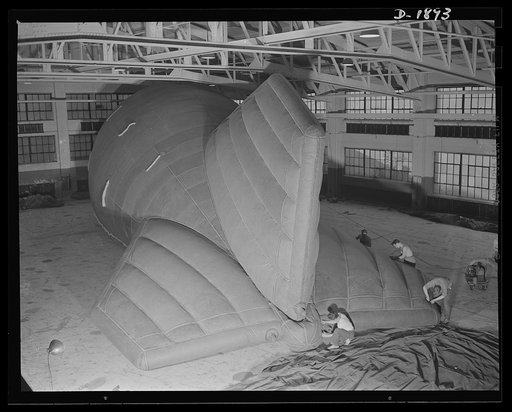 Barrage balloon manufacture. Reinforcing tail rigging of a new ballonet type barrage balloon, these workers at the barrage plant are cementing, seaming and rolling reinforcing tape across points in the tail and fins where strain is greatest. General Tire and Rubber Company, Akron, Ohio