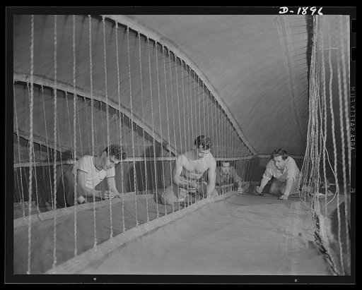 Barrage balloon manufacture. Fin-shaping cords. These workers are inside the rear-right horizontal fin of a barrage balloon, checking the ropes which give the fin shape and hold it together. Since barrage balloons are non-rigid and entirely collapsible, these ropes come closest to being the "back-bo