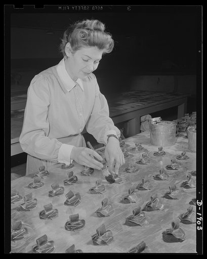 Assault boat Production. Building assault boats for U.S. Marine Corps. Woman worker in balloon room applies rubber cement to fittings through which hand ropes will be strung around outer circumference of boat. Goodyear, Akron, Ohio