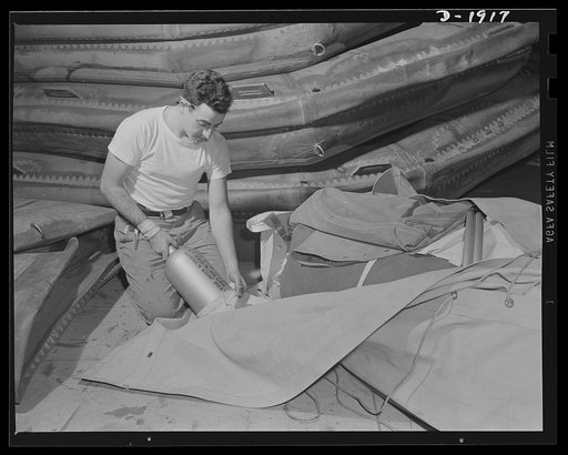 Assault boat Production. Building assault boats for U.S. Marine Corps. Workmen in the balloon room is inserting compressed gas bottle used for inflation of boats in the container preparatory to packing boat for shipment. Goodyear, Akron, Ohio