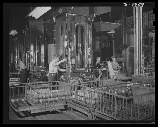 Three-inch A.A. cartridge cases. Cartridge cases for three-inch antiaircraft shells go through the first drawing operation. A brass cup formed from flat disc is fed to a huge press which draws it into a tubular shape with one rounded closed end. Washing and annealing precedes the first draw and will