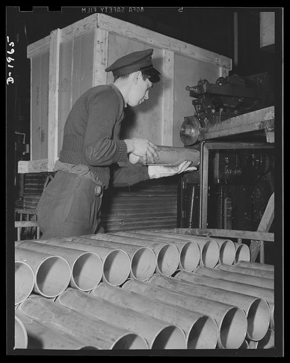 Three-inch A.A. cartridge cases. Beginning as a flat disc, the antiaircraft case is now advanced to a tubular shape of increased length and is nearly ready for the third draw that will lengthen it still more. Before the drawing operation a plant workman gives it a rough trim