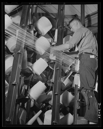 Tying in new spools. This is a highly skilled occupation, and is supervised at this tire company by a man whose previous training was in a weaving mill in Scotland. The deft weaver's knot, which will not pull out, must be tied in the fraction of a second whenever a break occurs, to catch the broken 