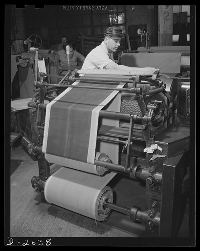 Wrapping in cloth prevents sticking. Reels of fabric may be stored for a few moments or a few days, wrapped in cloth to prevent it from sticking to itself when rolled up. These reels are brought from storage to machines such as this, in which the fabric is out on a powered bias cutter to exact lengt