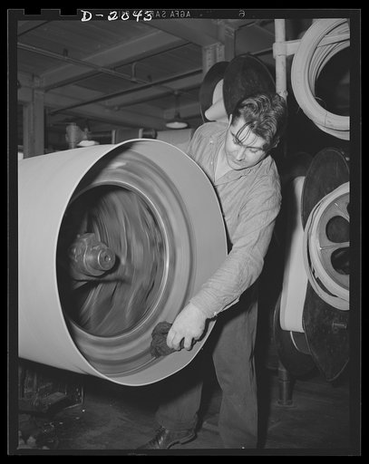 Shaping the sidewall. Moistening the bead area with a special rubber solvent and cement, the tire builder makes ready to force the overhanging edges down and around to the bead where it will first be anchored, then trimmed. The wheel spins and stops by foot control, leaving both hands free for work 