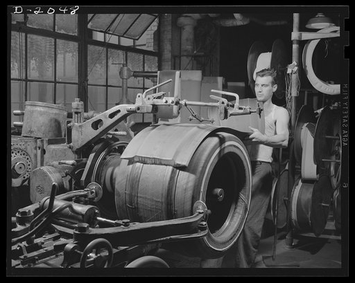 Adding tread rubber stock. When the fabric carcass has been built to the proper number of layers and cushion rubber has been added under the tread, the thick, extra tough tread rubber is added, having been molded to the proper shape by extrusion in a previous operation. Mechanical guides help this b