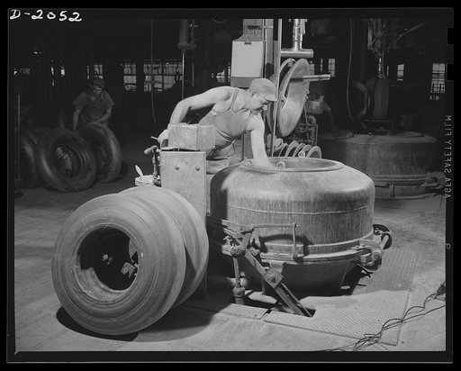 Vacuum shaping machine. Flat carcasses taken from the storage racks are placed in this vacuum machine in which two things happen. First a combination vacuum suction and squeezing action pulls the tire into the shape it will always have in use. Second, an airbag is forced into the inside to provide i