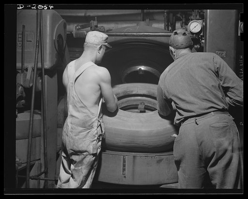 Putting tire into curing mold. From the vacuum expander, the potential new truck tire is taken to this "watch-case" curing mold in which it is baked under high heat and pressure for a long time. The exact time and temperature varies with the type and size of tire. The airbag inside the carcass is fi