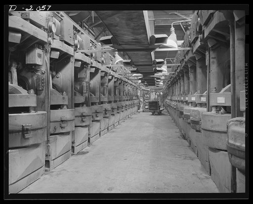 Battery of curing molds. While the curing, or cooking, operation is going on for the tire we have followed through the plant, it is also going on simultaneously for hundreds of other tires in production. This view shows one corridor in the curing room where fifty tires are being cured at once. Addit