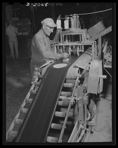 Adding valve patch and stamping. As the endless tube passes by, the proper length of each tube is automatically crimped into the edge, and serves as a guide for placing the valve patch and stamping the trade name. This tire worker operates both sides of this machine....places the patch into position
