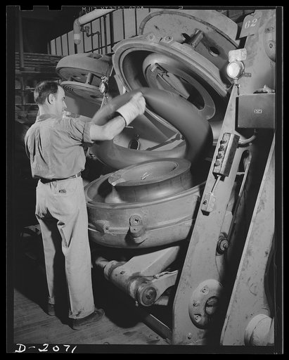 Removing cured tube from mold. As the tire molds are all-automatic, so are the tube molds. This one has just opened; all the operator need do is remove the finished tube and put in another raw one. Note the seam marks in the mold itself, which leave their imprint on the tube. Thus a seamless tube ma