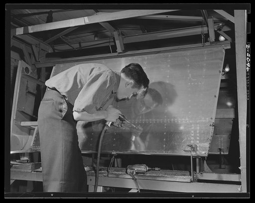 Subcontracting aircraft parts. This riveter is applying the finishing touches to highly-polished surface of a portion of aircraft sub-assembly at an Ohio plant. Goodyear, Akron, Ohio