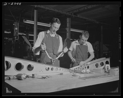 Subcontracting aircraft parts. Many strange-looking tools are required to get into the difficult places where rivets must be placed in the modern military airplane. Workers are working on an airplane sub-assembly part in an Ohio plant. Goodyear, Akron, Ohio