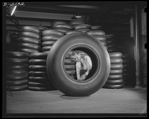 Aircraft tire manufacture. Inspector in rubber factory checks large airplane tire prior to preparation for shipment. Stack of airplane tires for a famous American fighter are shown in background. Goodyear, Akron, Ohio