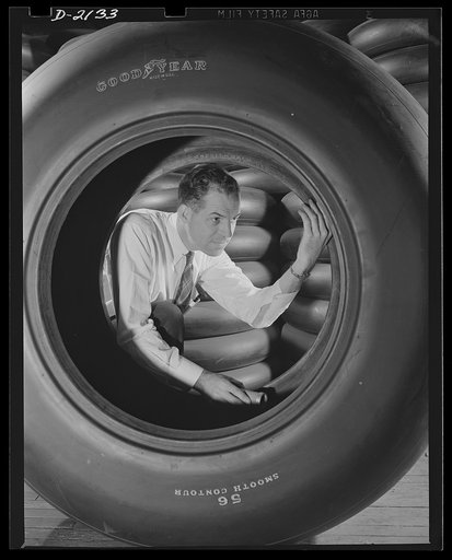 Aircraft tire manufacture. Inspector in rubber factory checks large airplane tire prior to preparation for shipment. Stack of airplane tires for a famous American fighter are shown in background. Goodyear, Akron, Ohio