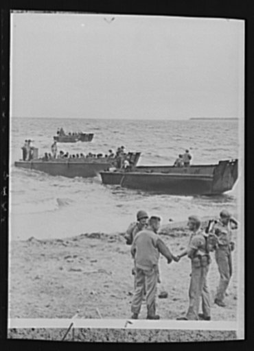 U.S. Marines say goodbye to Guadalcanal. A newly-arrived U.S. Army soldier shakes hands in farewell to a U.S. Marine about to board the waiting barge for transit to a troop ship lying out in deeper water. This scene took place on the beach of Guadalcanal Island in the Solomons as the Marines turned 